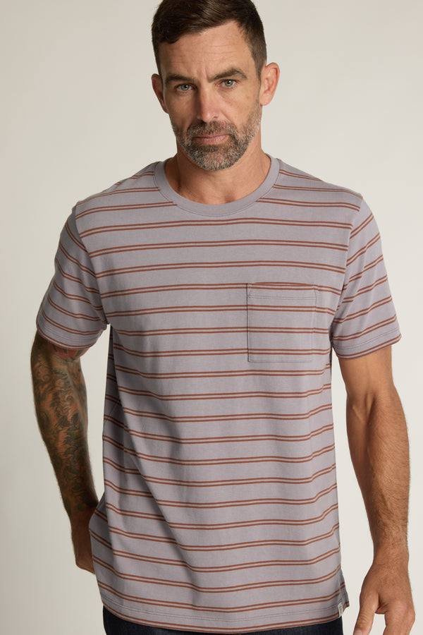 A man with short brown hair and a beard wears the Barkers Talbot Stripe Tee, featuring thin red horizontal stripes and a chest pocket, standing against a plain light background.
