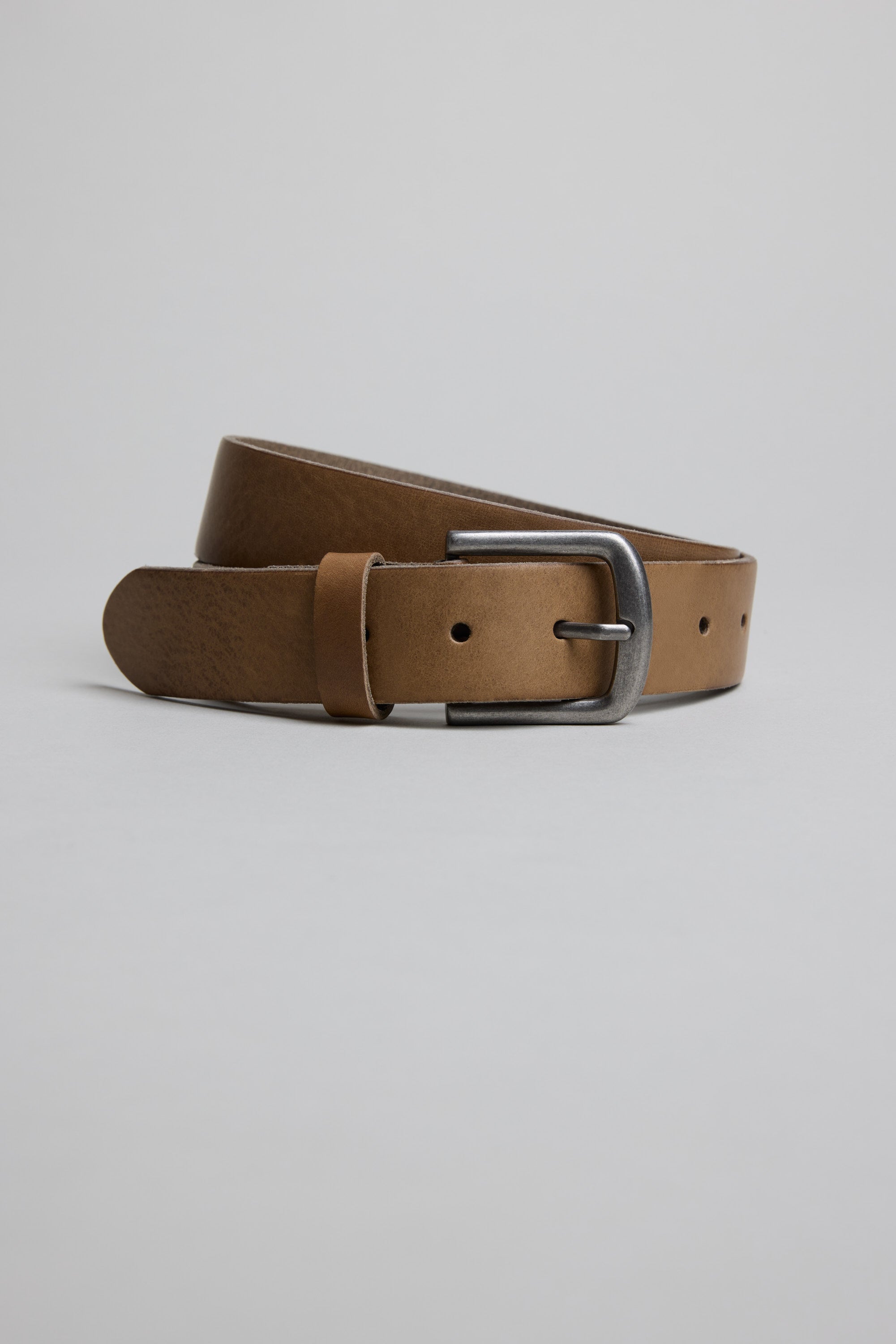 The Parisian Tuscany Leather Belt, made in New Zealand from genuine brown leather, features a silver buckle and is coiled neatly on a plain light gray background.