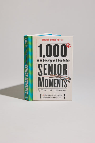 A standing copy of "1000 Unforgettable Senior Moments" by Other, a humorous book with glasses on the cover and a blue-green spine, photographed against a plain light gray background. A great gift idea for seniors.