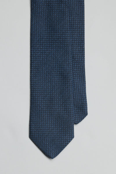 The Parisian Lunan Texture Tie by Parisian is shown in navy blue with a subtle textured pattern, neatly arranged against a light gray background and the pointed tip facing downward. This tie is handmade in New Zealand.
