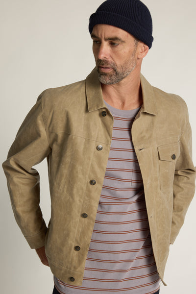 A man in the Barkers Talbot Stripe Tee, tan button-up jacket, and navy knit beanie looks to the side with his hands on his hips.