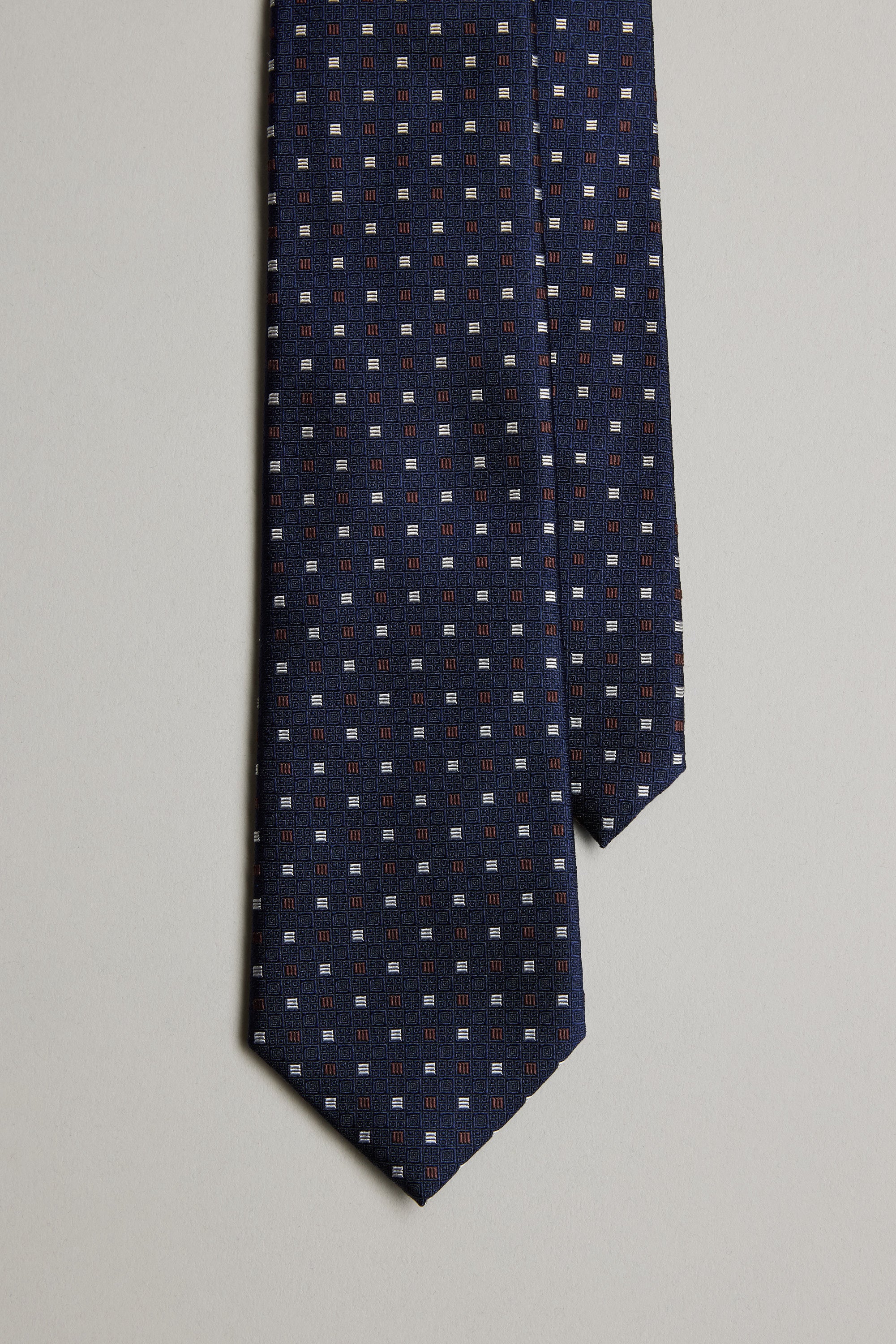 The Larwin Square Tie by Barkers is a navy blue silk accessory with a jacquard square pattern in light blue, white, and red—perfect for refined business attire. Shown against a light gray background.