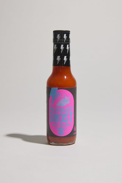 A bottle of Culley's Malevolent Ghost Hot Sauce stands upright on a light surface, its black label with pink and blue graphics. Made with Naga Jolokia peppers, this sauce from Culley's delivers fiery flavor in every drop.