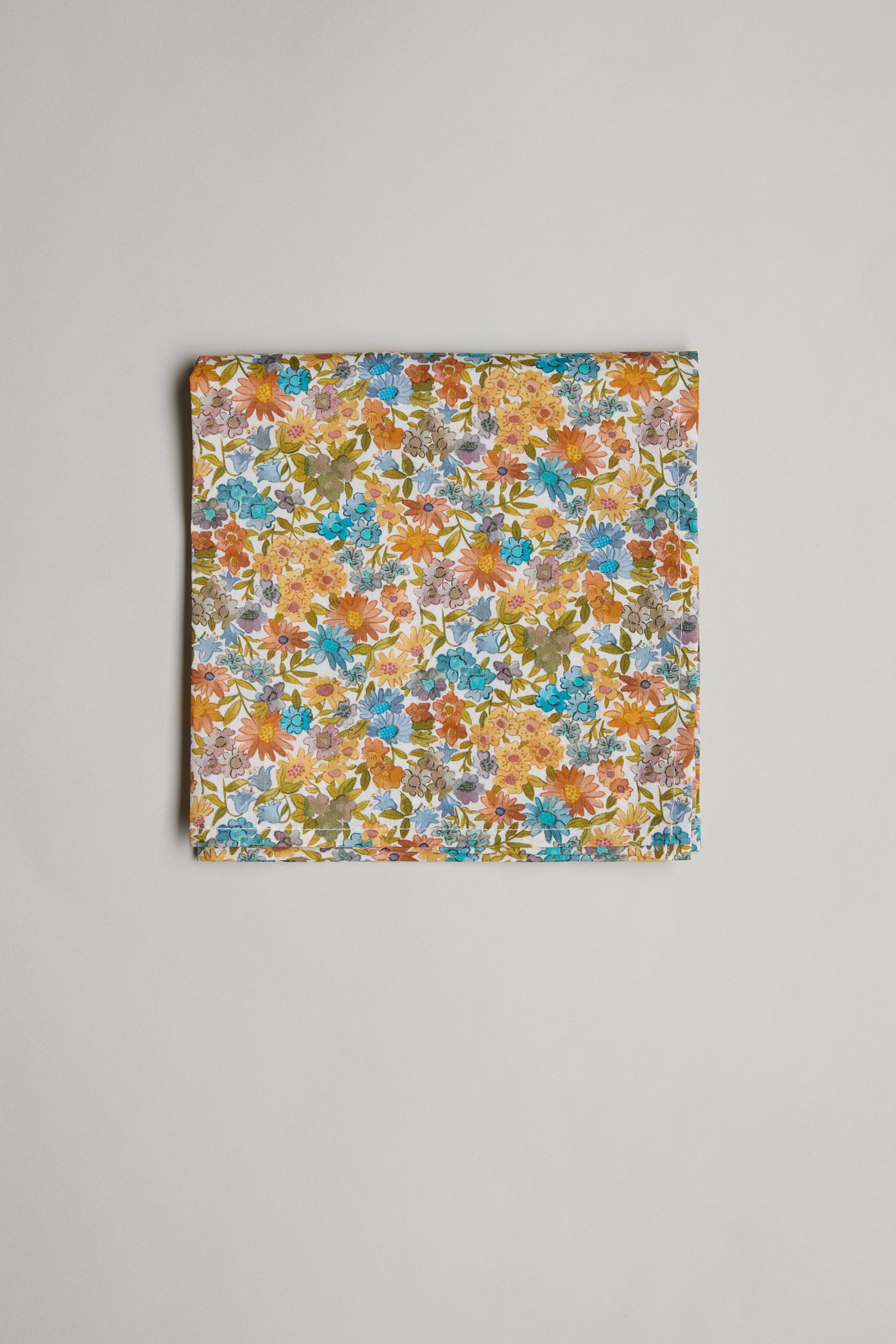 A folded piece of Liberty Sandra Spring PS Tana Lawn cotton fabric by Liberty features a vibrant floral print with orange, blue, yellow, and green flowers, displayed on a plain light background.