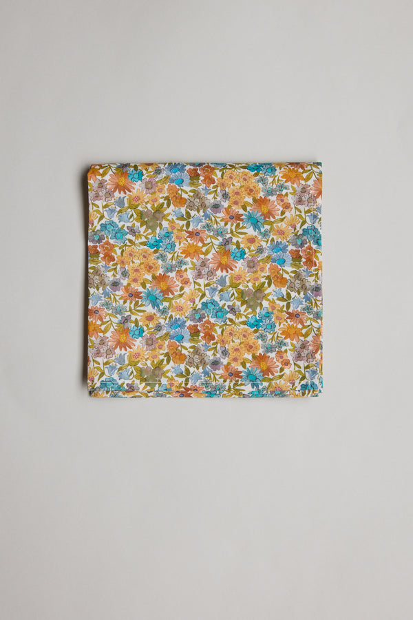 A folded piece of Liberty Sandra Spring PS Tana Lawn cotton fabric by Liberty features a vibrant floral print with orange, blue, yellow, and green flowers, displayed on a plain light background.