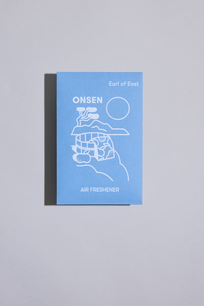 The EoE Onsen Air Freshener by Earl of East comes in a blue rectangular package with minimalist white mountain, sun, and water line art—a stylish, portable fragrance for any space.