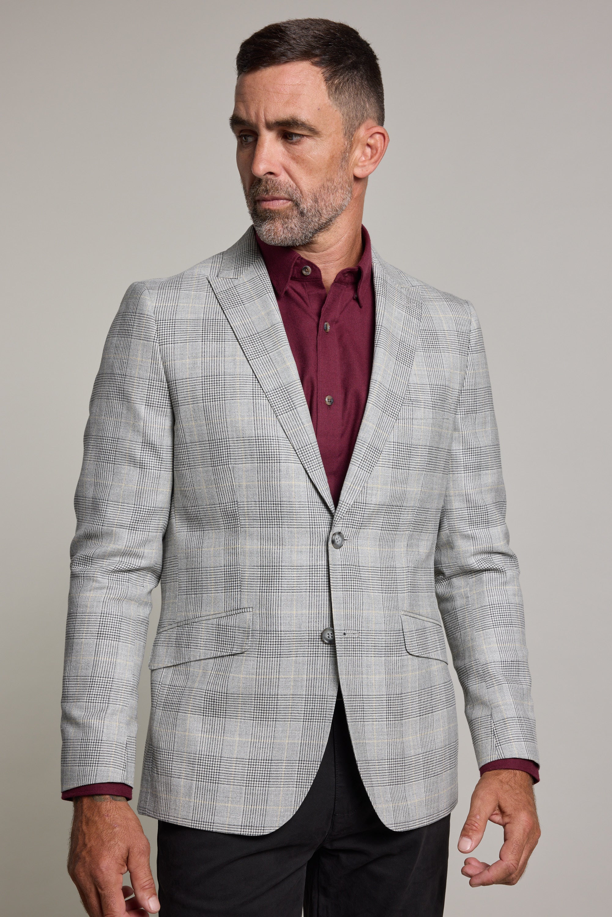 A man with short dark hair and a beard wears the Barkers Remsen Check Blazer over a burgundy shirt, standing against a plain light background and gazing to his left.