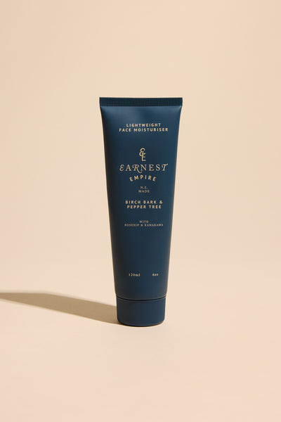 A dark blue tube of Other Earnest Empire Lightweight Moisturiser stands upright on a beige surface. The label highlights hydration with rosehip oil, birch bark, pepper tree, and nourishing manuka honey.