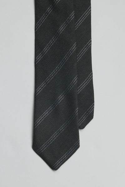 A close-up of the Parisian Jura Stripe Tie by Parisian, a handmade black tie featuring subtle diagonal white stripes, displayed on a plain light gray background.
