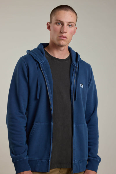 A young man with short hair wears a dark blue Barkers Newton GD Zip Hoody over a black t-shirt against a plain, light background. He looks at the camera with a neutral expression, highlighting the year-round comfort of the hoodie.