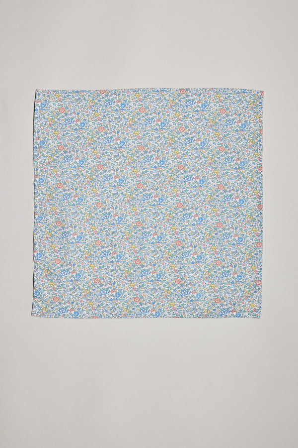 The Katie and Millie Liberty PS by Liberty is a square pocket square featuring a dense floral pattern in blue, yellow, orange, and green on a white background, shown laid flat on a plain light surface.