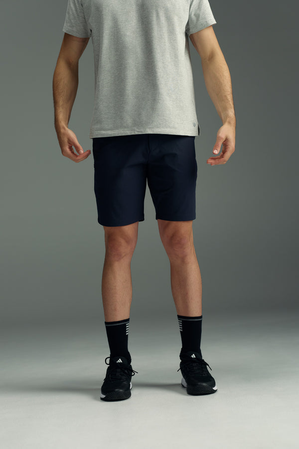 A person stands against a gray background, wearing a light gray t-shirt, WearEver Switch Short by WearEver in dark navy, black crew socks, and black athletic shoes. The head is not visible in the image.