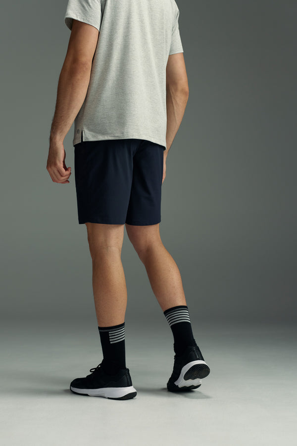 A man faces away, wearing a light gray T-shirt, black sneakers, black socks with white stripes, and WearEver Switch Shorts by WearEver in dark navy, standing against a plain gray background.
