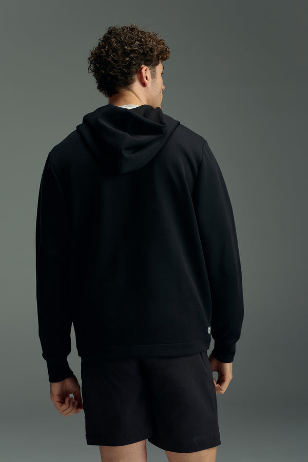 A person with curly hair stands facing away from the camera, wearing a black WearEver Altitude Hoody by WearEver and black shorts, set against a plain gray background.