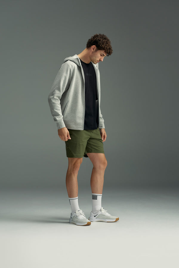 A man stands in profile against a gray background, wearing the WearEver Altitude Hoody by WearEver, a black t-shirt, olive green shorts, white crew socks, and white sneakers while looking down.