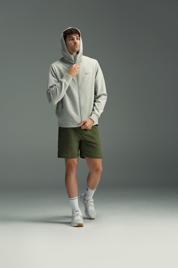 A man wearing the WearEver Altitude Hoody in light gray, paired with olive green shorts, white crew socks, and gray sneakers, stands against a plain gray background, looking to the side while adjusting his hood.