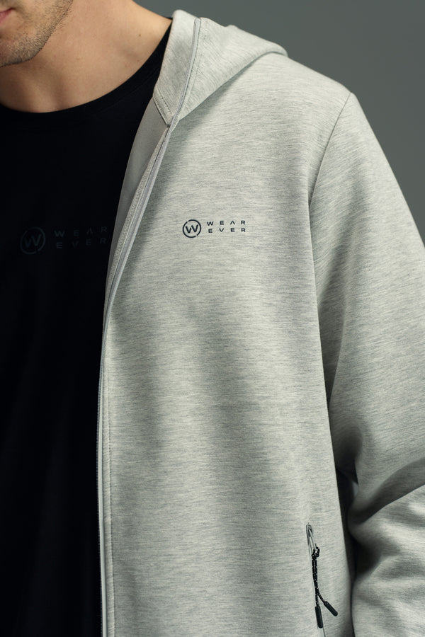 A person wearing a light gray WearEver Altitude Hoody with a small logo on the chest and a black t-shirt underneath. The image, showing only from the shoulders to mid-torso, highlights the lightweight design by WearEver.