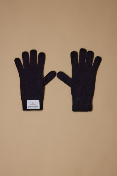 A pair of black NZ Made Perino Gloves by Woolyarns Perino, crafted from a merino possum silk blend, lay flat on a light brown surface with a white label sewn onto the wrist of the left glove. Made in New Zealand.