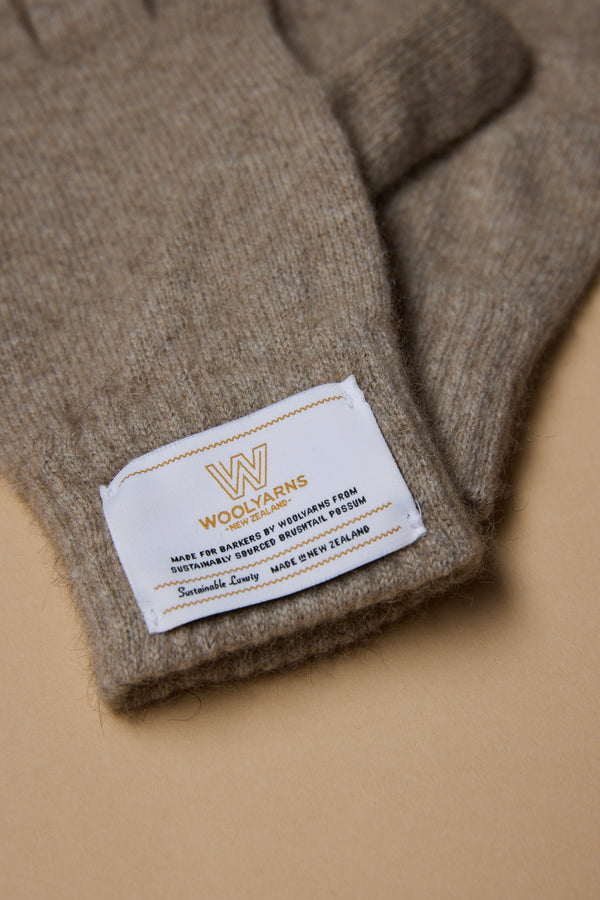 A close-up of NZ Made Perino Gloves by Woolyarns Perino, featuring a white fabric label and crafted from sustainable, biodegradable merino wool in beige.