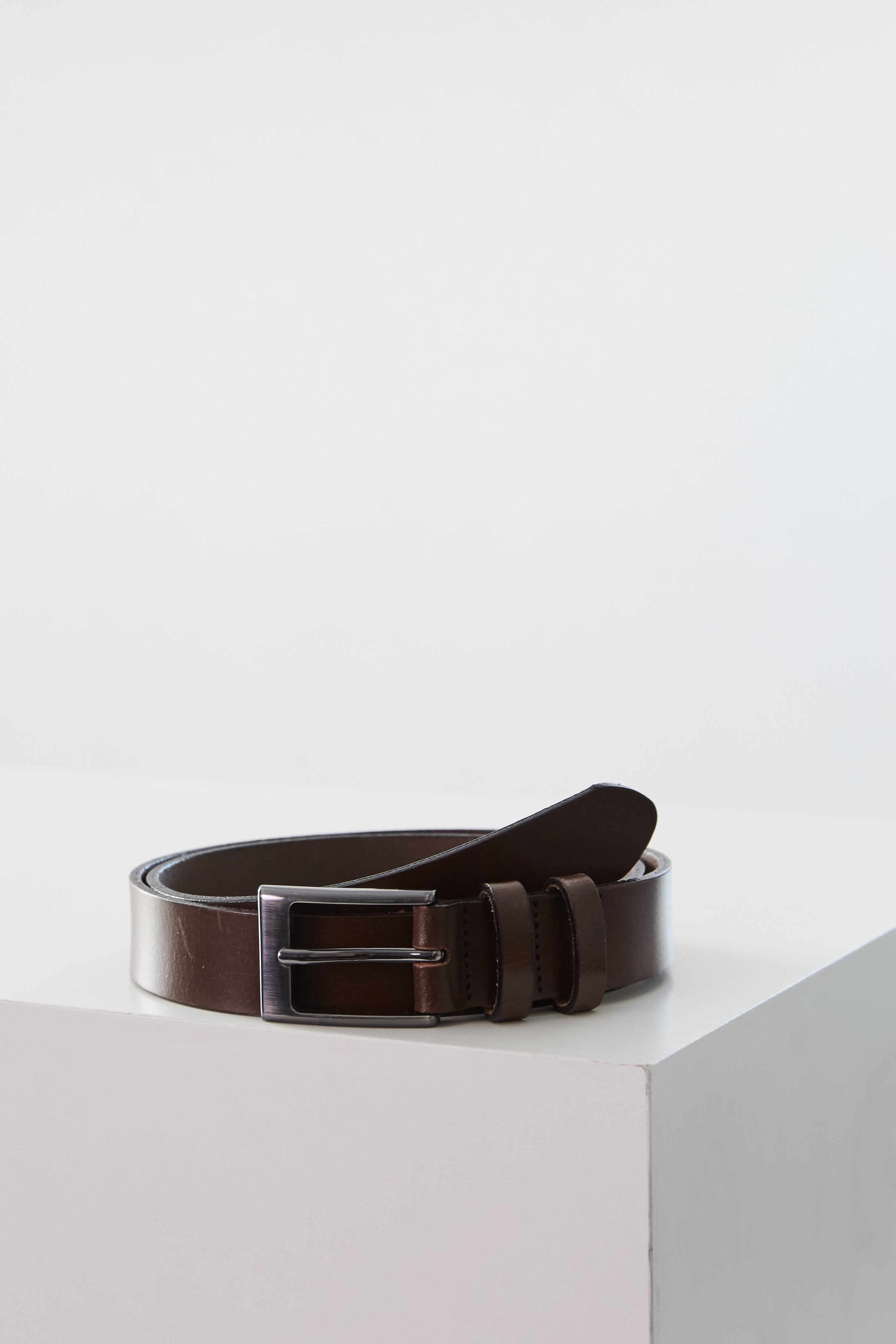 The Barkers Frances Leather Belt, in dark brown with a square buckle, is coiled neatly on a white surface against a plain light background.