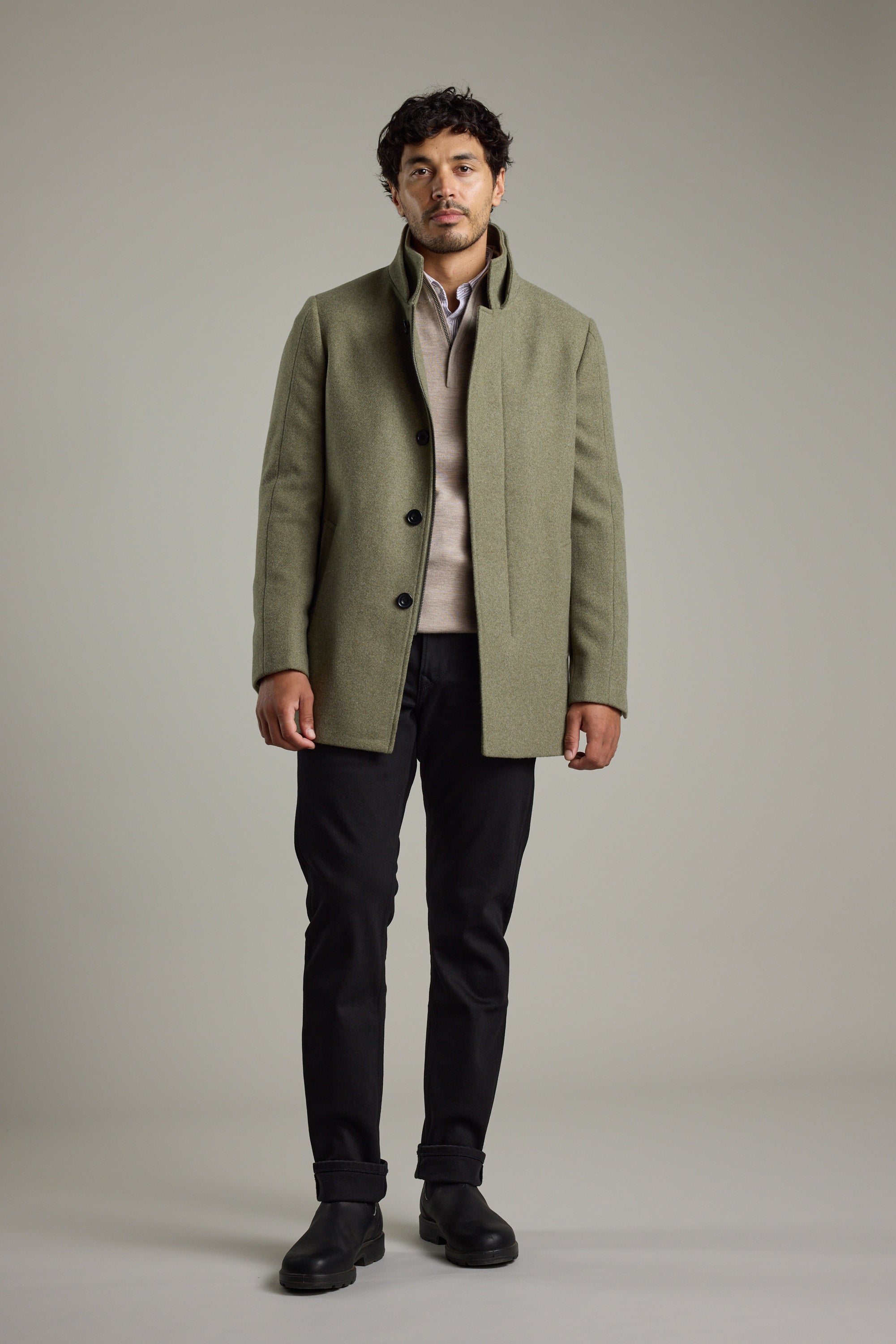 Man wearing a Barkers Raymond Coat, beige sweater, black pants, and black boots, standing.