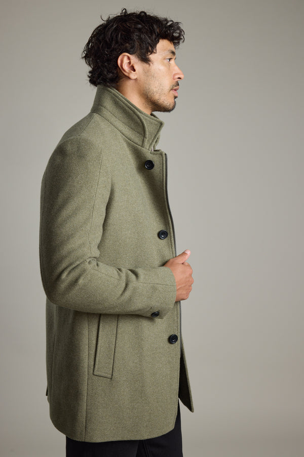 Man in a green Barkers Raymond Coat stands sideways against a plain grey background.