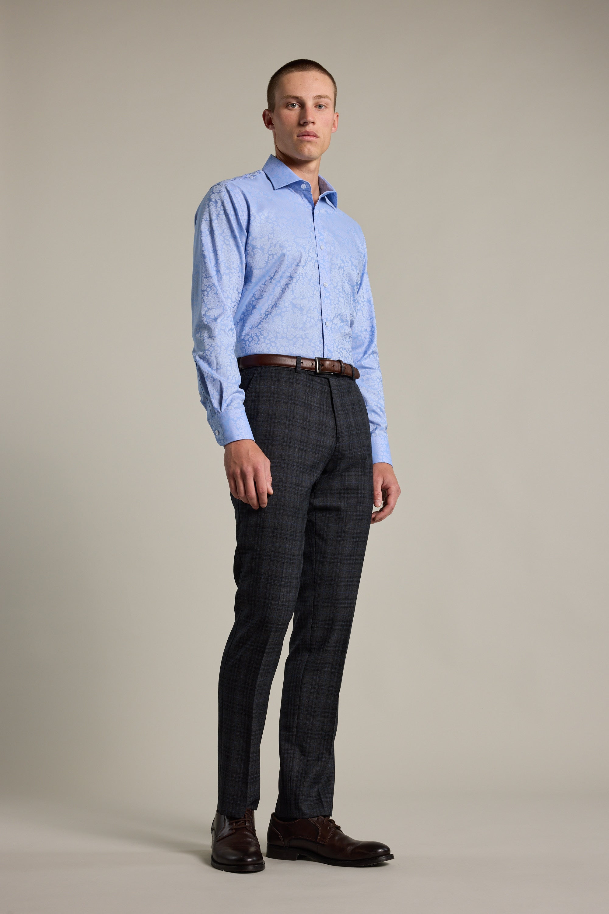 A man stands facing forward, wearing the Barkers Corran Paisley Business Shirt in a tailored fit, tucked into dark plaid dress pants with a brown belt and dark dress shoes, against a plain light background.