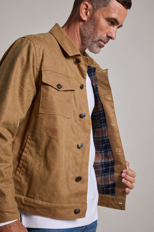 A man with short hair and light stubble holds open a Barkers Benson Waxed Cotton Jacket, revealing its plaid lining. He wears a white shirt underneath.