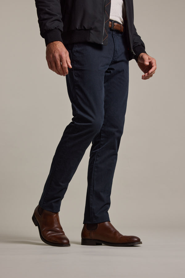 Wearing Barkers Carnaby Chinos in dark blue, a black jacket, white shirt, brown belt, and brown leather Chelsea boots, the person stands against a plain light background.
