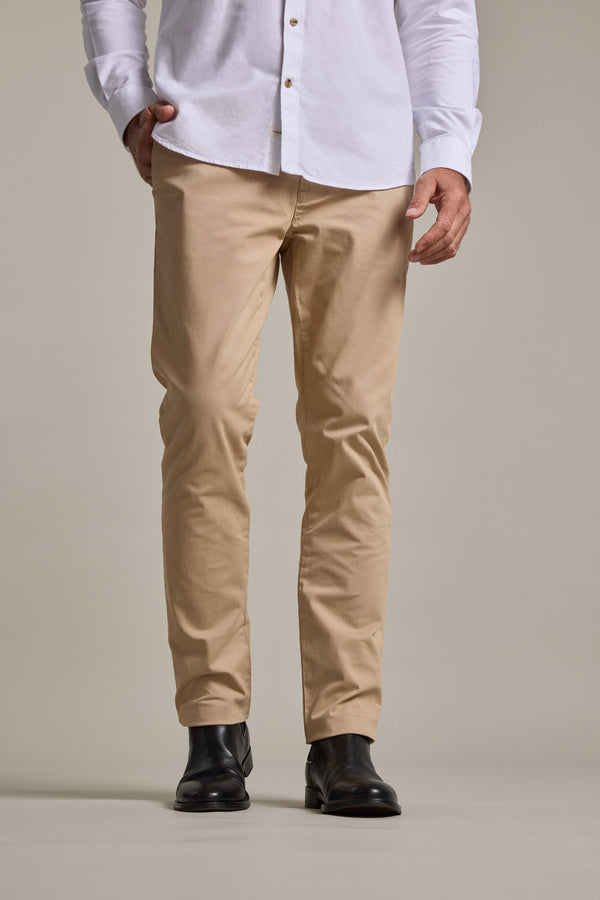 A person wears Barkers Carnaby Chino men's stretch chinos, made from responsibly sourced cotton, with black leather shoes. Standing against a plain neutral backdrop, the image is cropped at the shoulders to show only the lower half.