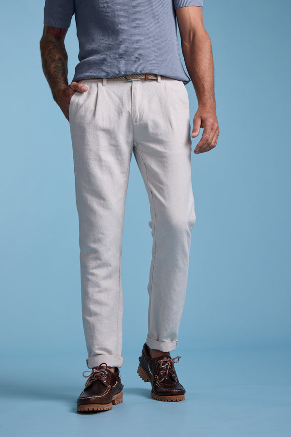 A man stands against a blue background wearing the Barkers Newman Linen Pant, paired with a light blue short-sleeve shirt and brown leather shoes. His hands are in his pockets, and only his body from shoulders down is visible.