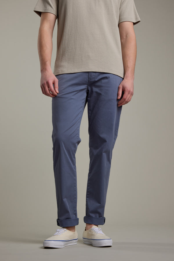 A person showcases the lower half wearing Barkers Kingly Chino Pant in blue with a beige short-sleeve shirt and white sneakers, standing against a plain neutral background. Only their lower body is visible.