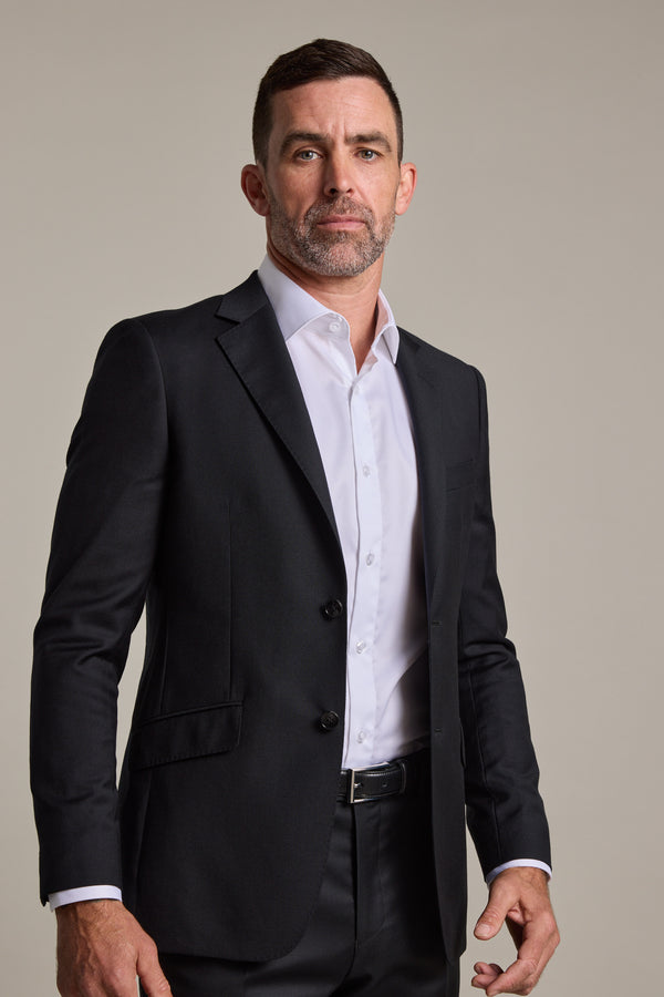 A man with short dark hair and a trimmed beard wears the Barkers Mayfair ZQrx Suit Jacket, crafted from fine merino wool, over a white dress shirt. He stands against a plain light background, looking confidently at the camera.