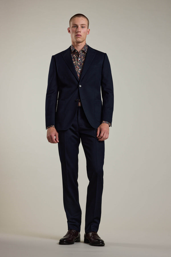 A man stands facing forward in a dark navy suit with a single-button blazer, Barkers Croydon Twill Suit Trouser, a colorful patterned shirt underneath, and dark dress shoes against a plain light background.