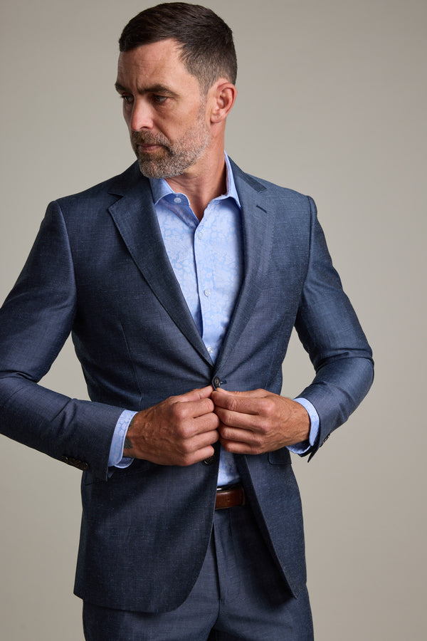 A man with short hair and a beard buttons the Barkers Charles Texture Suit Jacket over a light blue dress shirt, highlighting modern tailoring as he looks to his left against a plain background.