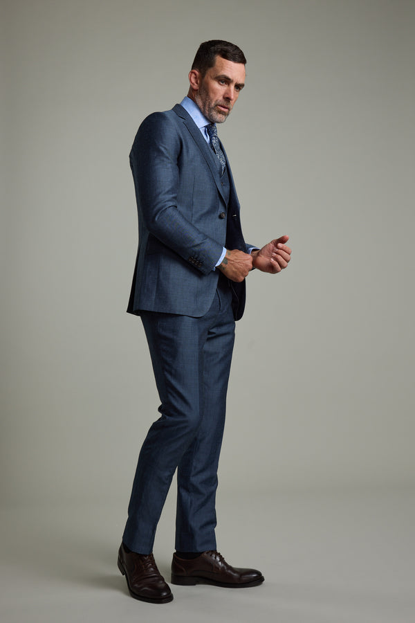 A man in the Barkers Charles Texture Suit Jacket, paired with a light blue shirt and patterned tie, stands in a studio adjusting his cufflinks—a modern tailoring statement against a neutral background.
