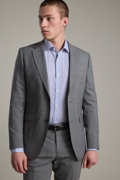 A man wearing the Barkers Henderson Houndstooth Suit Jacket over a light blue patterned dress shirt stands against a plain background, looking slightly to his left.