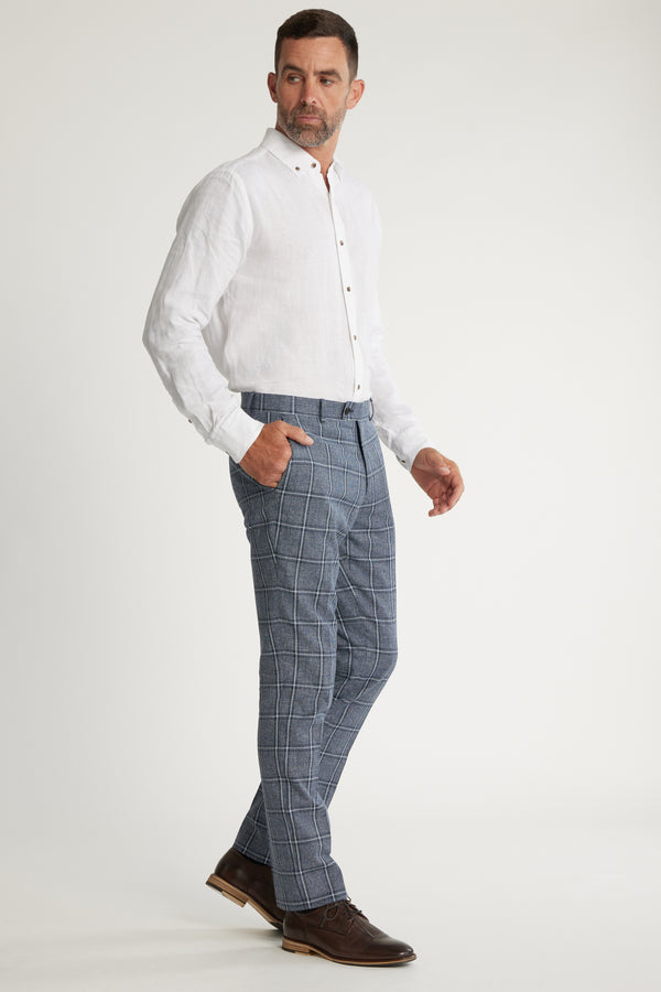 A man stands in a relaxed pose wearing a white button-up shirt, Barkers Highland Check Suit Pant, and brown dress shoes against a plain white background.