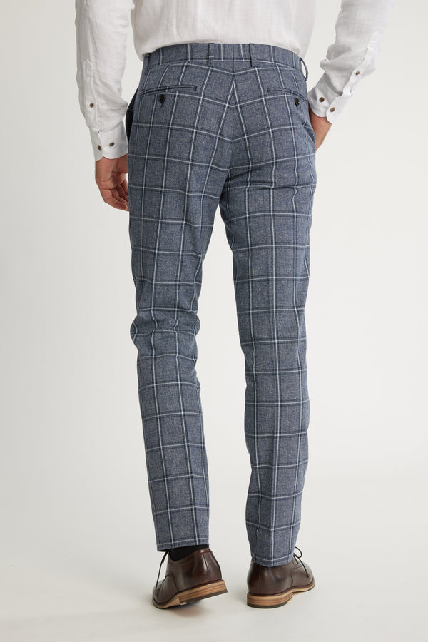 A person is shown from the back, wearing Barkers Highland Check Suit Pant in blue plaid with a white long-sleeve shirt and brown dress shoes, set against a plain light background.