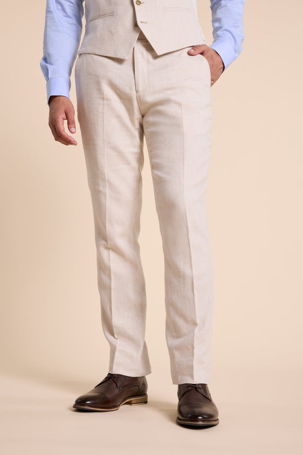 Man in Barkers Thompson Textured Linen Pant, blue shirt, brown shoes stands hands in pockets.