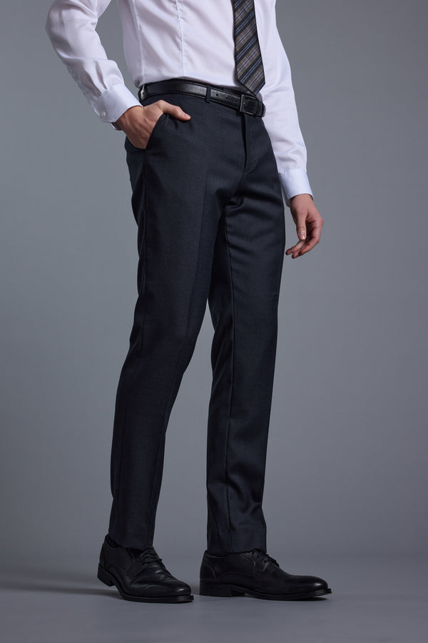 Wearing the Barkers Mayfair ZQrx Suit Trouser with a white dress shirt, striped tie, black belt, and black dress shoes, a person stands with one hand in their pocket against a plain gray background.