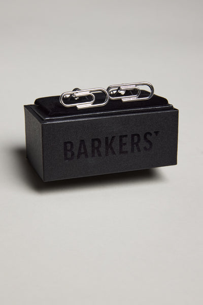 The Barkers Paper Clips Cufflink, featuring a polished silver finish, is displayed on a black box with the Barkers logo—perfect for adding elegance to French cuff shirts. The set rests on a light-colored surface.