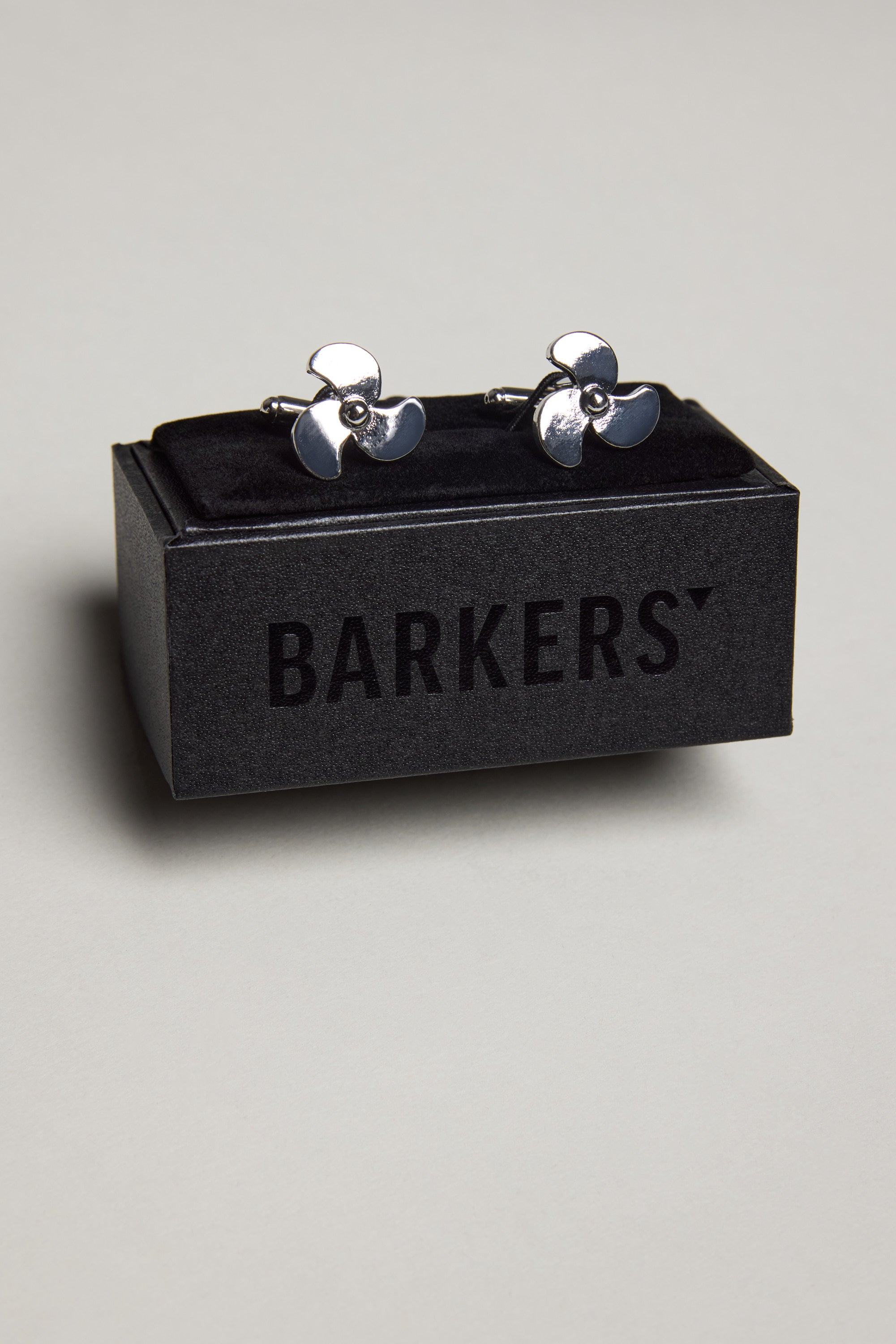 A pair of Barkers Propeller Cufflinks in silver tone, presented in a black velvet box with "Barkers" on the front—perfect for those who appreciate nautical style.