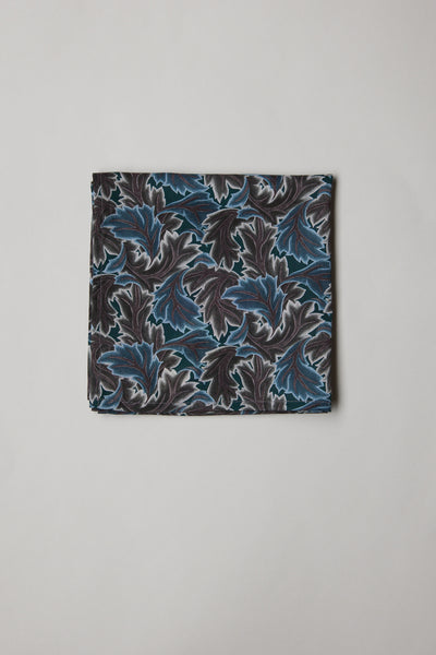 The Liberty Midnight Canopy PS by Liberty is a folded pocket square made from Tana Lawn cotton, showcasing a blue and grey leaf print on a light background.