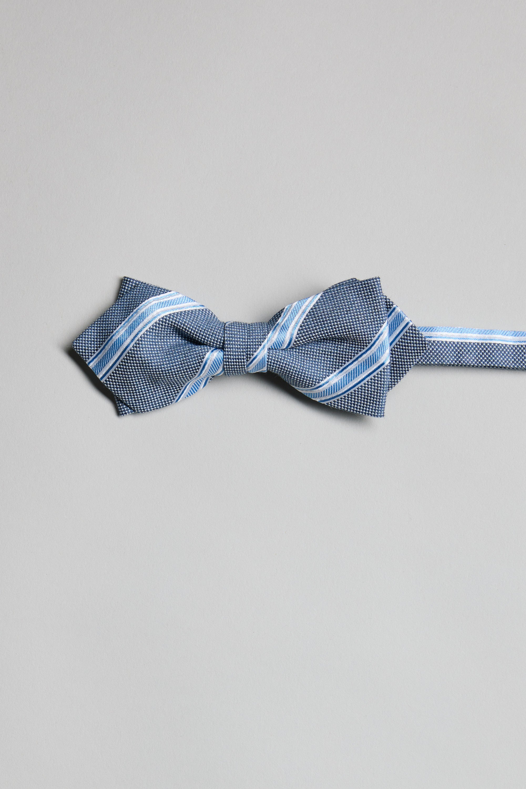 The Parisian Stripe Bow Tie by Parisian features blue with white and light blue diagonal stripes. Expertly handmade in New Zealand, it’s shown on a plain light grey background.