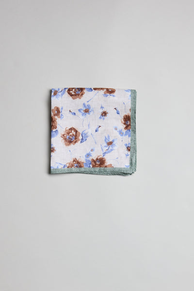The Parisian Floral Linen PS by Parisian is a neatly folded linen pocket square with a white base, brown and blue floral patterns, and a green border, displayed on a plain light gray surface.