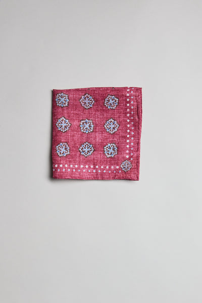 The Parisian Motif Linen PS by Parisian, a folded red linen pocket square with white decorative patterns and small floral motifs, is displayed on a plain light grey background.
