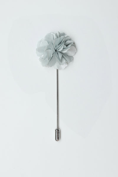 The Parisian Fraser Flower Lapel Pin features light gray layered fabric petals and a long silver stick pin, ideal as a suiting accessory for formal events. Shown on a plain white background.