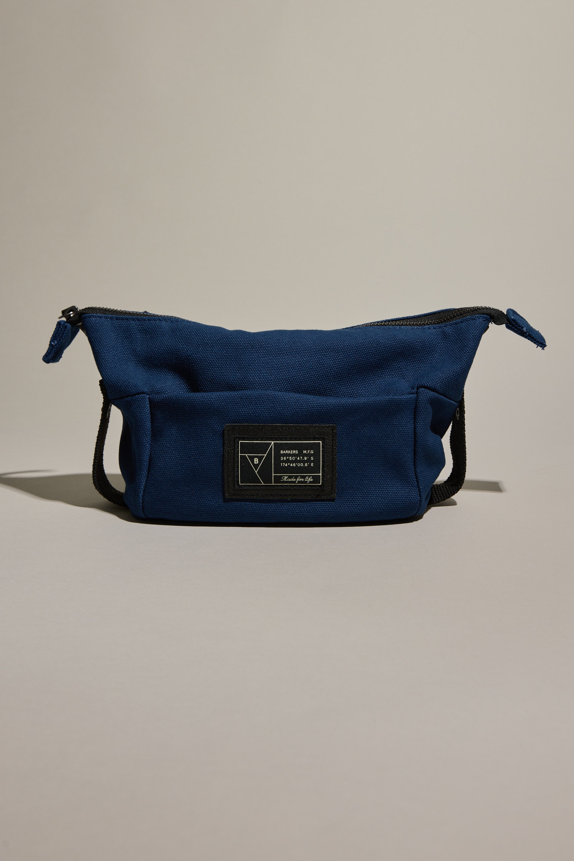 The Barkers Canvas Toiletry Bag is a blue fabric bag with a black zipper and a black rectangular patch featuring white text and graphics on the front, shown against a neutral background.