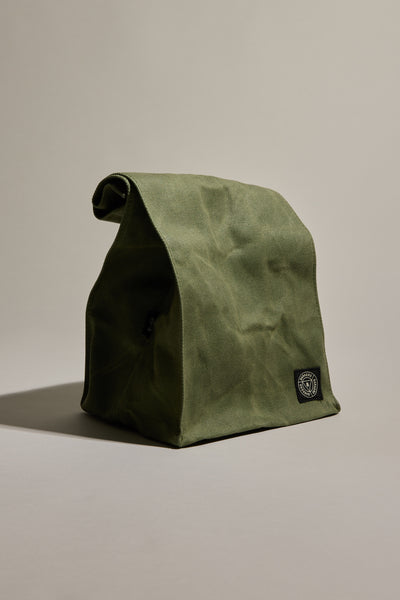 The Barkers Waxed Lunch Bag in green cotton canvas features a folded top and a black and white logo patch on the lower front, offering a stylish and durable way to carry your lunch.